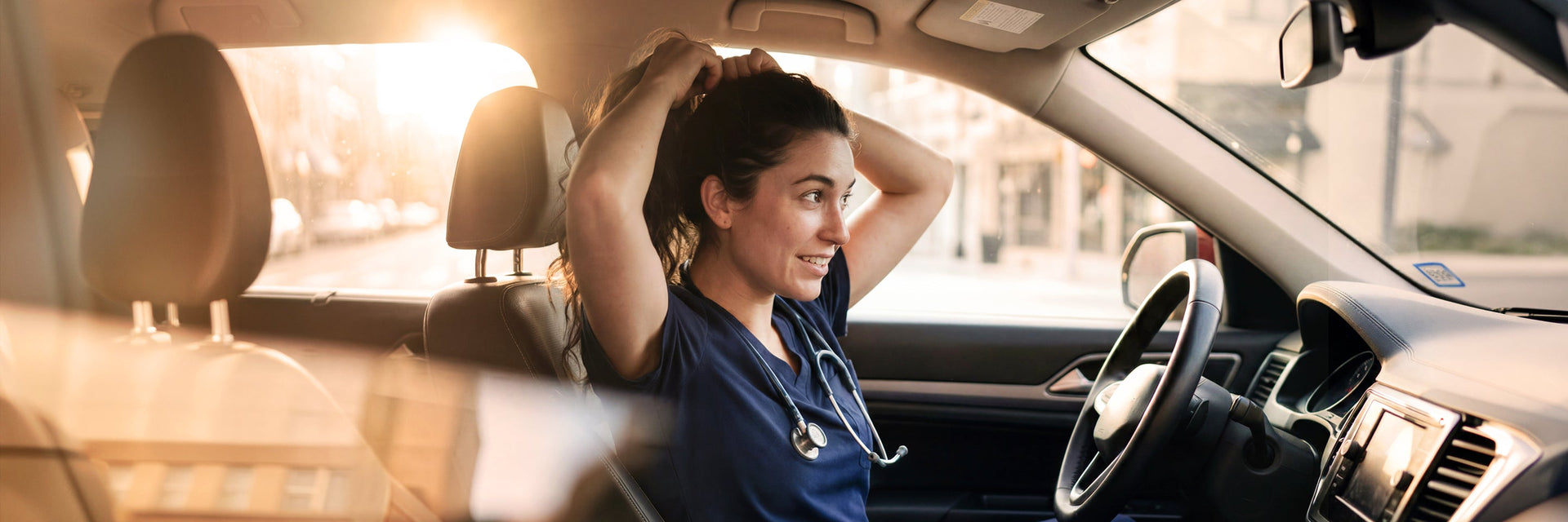 A male healthcare professional in dark scrubs sitting in the drivers seat of a vehicle